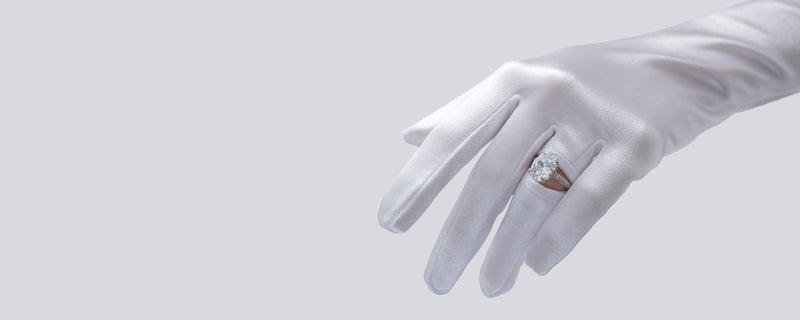 Hand wearing a white glove holding a ring with a diamond on a light gray background