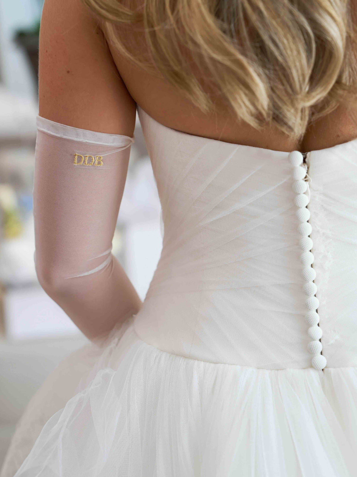 Sheer white bridal opera glove monogrammed with gold initials, worn with a tulle wedding dress