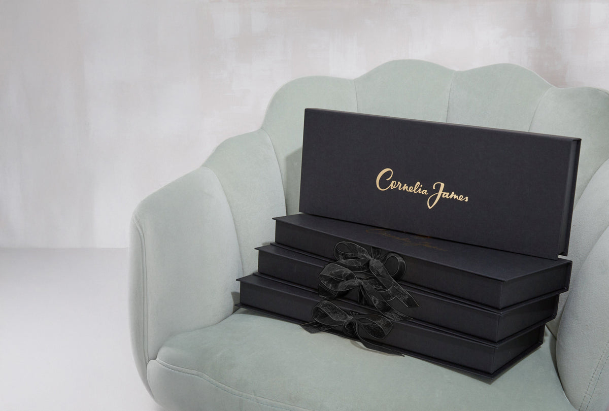 Stack of black boxes with 'Cornelia James' branding on a light green chair.